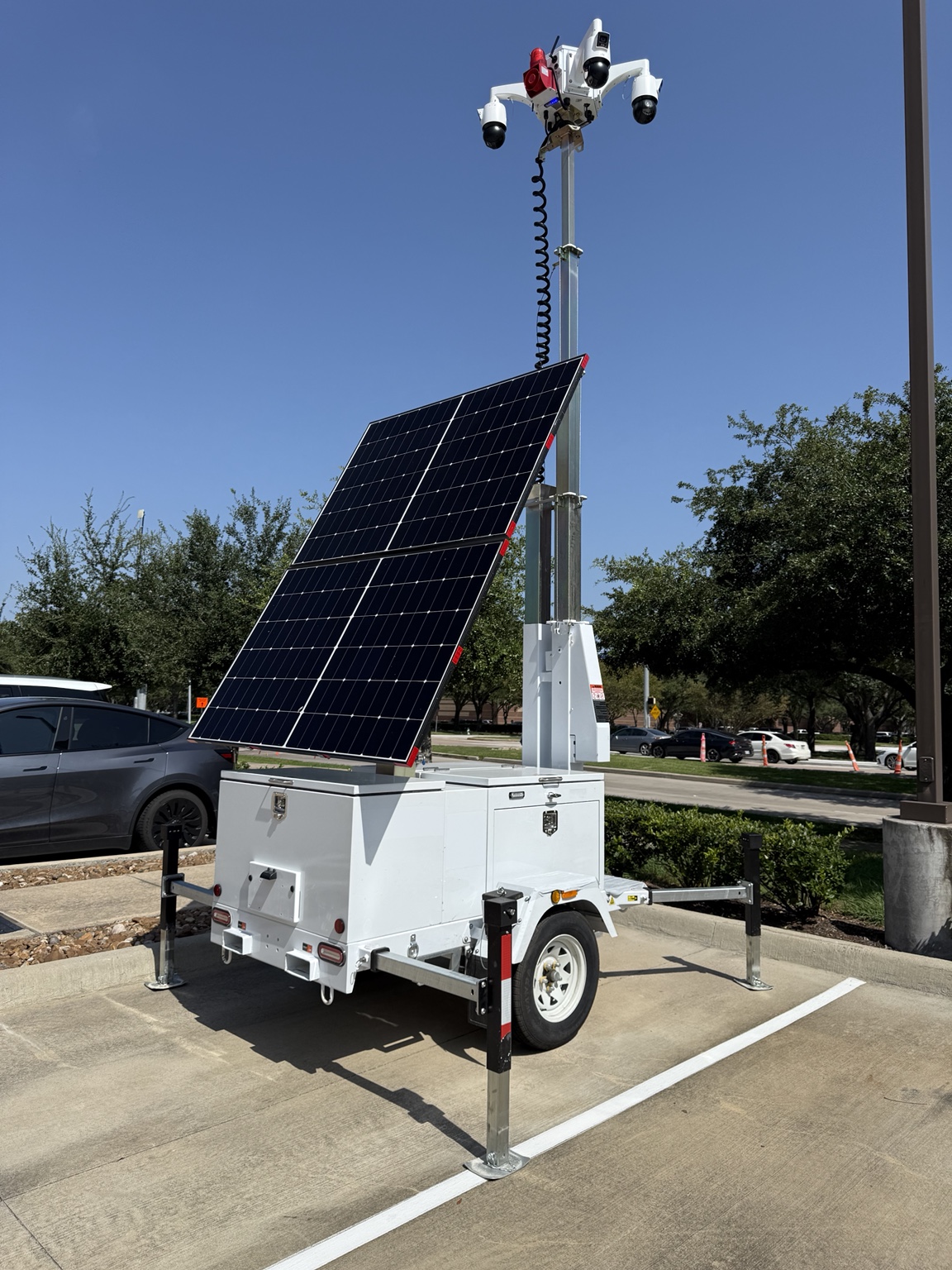 Mobile surveillance trailer with an elevated camera mast, solar panels, and stabilizers.